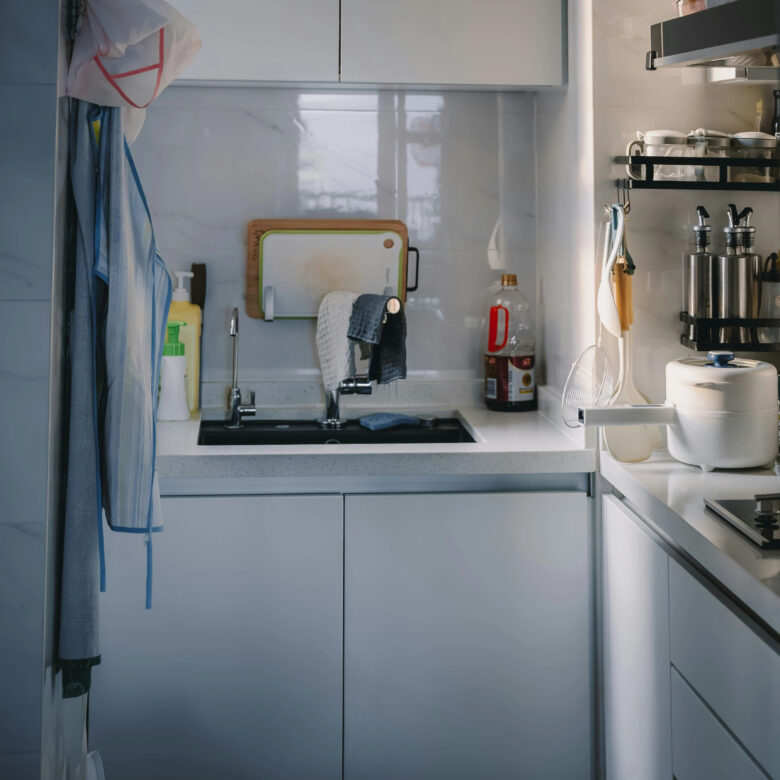 Pia de cozinha moderna e limpa com torneira de inox, detergente amarelo, panos de prato pendurados e suporte de parede com temperos organizados sob luz natural.